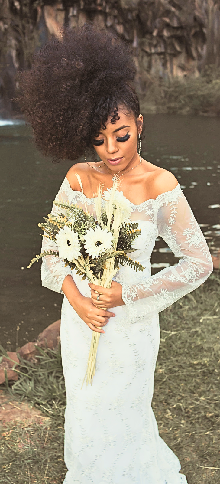 Photo libre de droits. Image d'une coiffure de mariée sur cheveux naturels. Mariée vêtue d'une robe blanche, se tenant au bord d'un lac avec un bouquet de fleurs dans les mains.